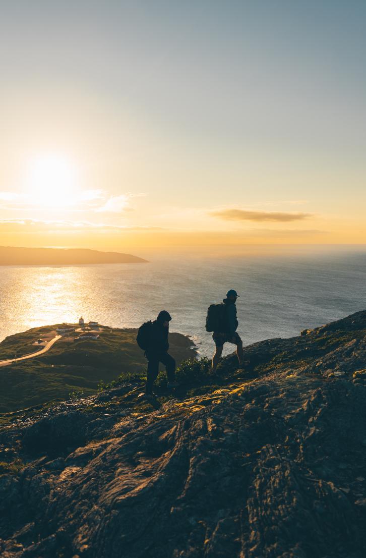 Hikers climbing a rocky hill at sunset by the ocean